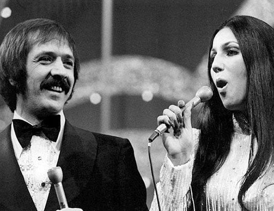 Sonny and Cher performing on stage together, singing with microphones during their famous 1970s TV show.