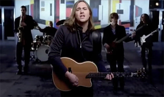 Lead singer of a band performing with an acoustic guitar, surrounded by bandmates playing various instruments, with a colorful abstract background.