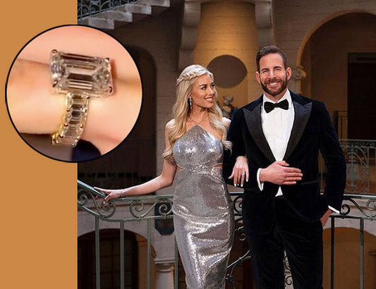 Couple posing together, with the woman wearing a sparkling silver dress and showing off her engagement ring with a large emerald cut diamond. The man is dressed in a tuxedo as they stand in a luxurious indoor setting.