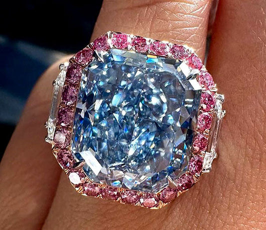 Close-up of a luxurious blue diamond ring with pink sapphire accents and white diamond side stones on a finger.