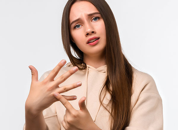 Young woman with long brown hair, wearing a beige hoodie, looking confused while holding up her hand and counting with her fingers.