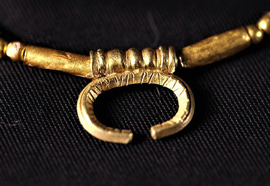 Close-up of an ancient gold necklace with a circular clasp and intricate detailing.