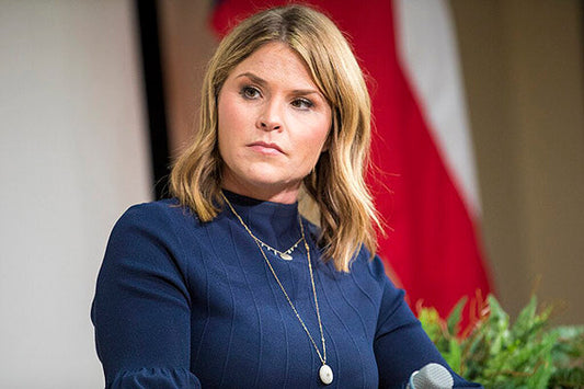 Jenna Bush Hager seated at an event with a thoughtful expression, wearing a blue blouse and pendant necklace.
