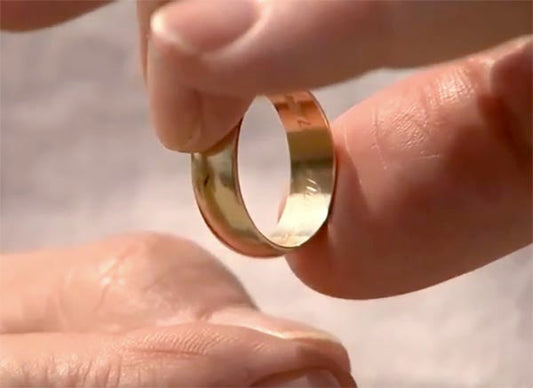 Close-up of a hand holding a gold wedding ring with a plain design.