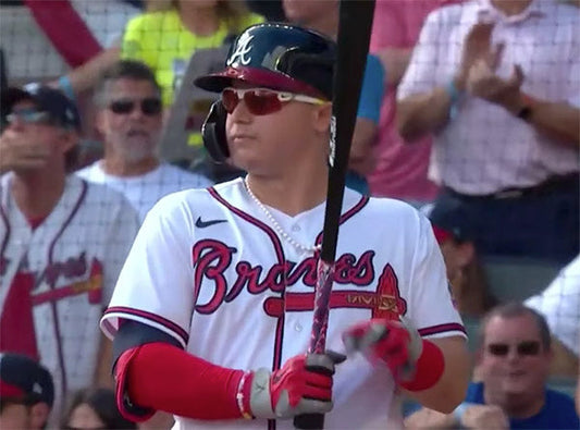 Baseball player wearing an Atlanta Braves jersey and sunglasses, holding a bat and preparing for a pitch during a game.