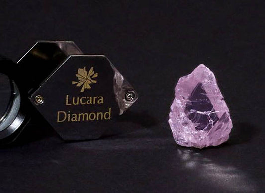Lucara Diamond logo with a raw pink diamond placed next to a magnifying loupe, showcasing the diamond's unique color and clarity.