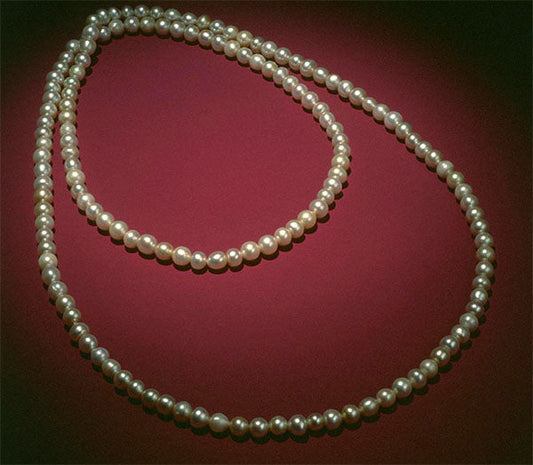 Two strands of elegant white pearls displayed on a rich burgundy background, highlighting their smooth, lustrous surface.