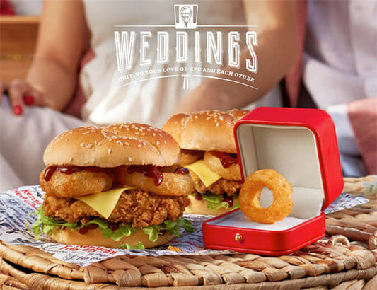 KFC wedding-themed promotional image featuring two chicken sandwiches with cheese and onion rings, and a red ring box with an onion ring inside, with the 'WEDDINGS' tagline.