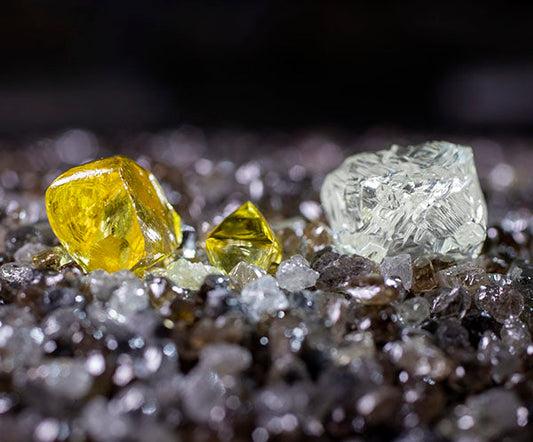 Raw yellow and clear diamonds surrounded by smaller rough diamonds, highlighting their natural beauty before cutting and polishing.