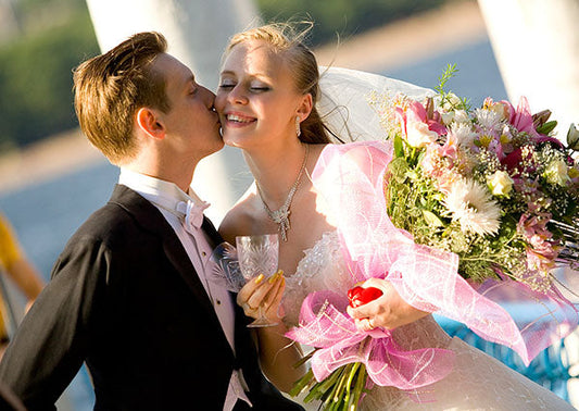 Happy newlywed couple sharing a kiss while the bride holds a beautiful bouquet of flowers, with a scenic background.