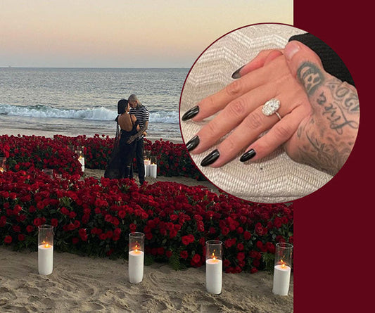 Couple engaged in a romantic beach proposal surrounded by red roses and candles, with a close-up of the woman’s hand showcasing an oval diamond engagement ring.