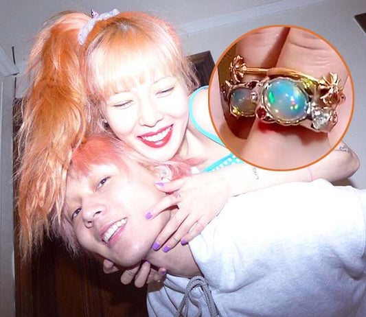 Young couple smiling and embracing, with the woman wearing a colorful outfit and a bright hairstyle. Inset image shows a close-up of the woman's opal ring, featuring two vibrant opal stones set in a gold band with floral accents.