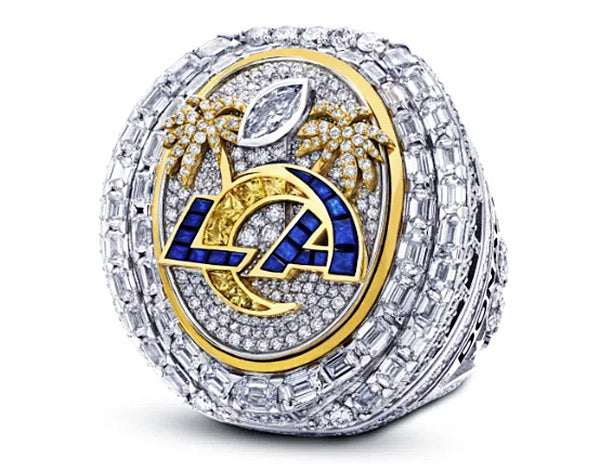 Close-up of a diamond-studded championship ring with the 'LA' logo and palm tree accents, set in gold and surrounded by sparkling diamonds, representing a sports achievement.