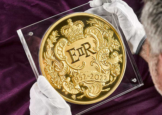 A commemorative gold coin featuring the emblem of Queen Elizabeth II (EIIR) with the years 1952-2022, being held carefully by a person in white gloves, showcasing the intricate design and royal insignia.