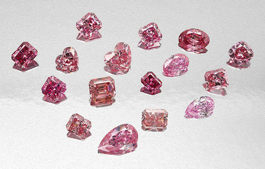 Collection of various pink diamonds of different shapes including emerald, heart, and pear cut on a reflective surface.