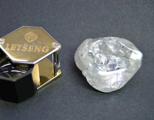 A large rough diamond from the Letseng mine next to a diamond holder, showcasing the diamond's natural raw form on a dark background.