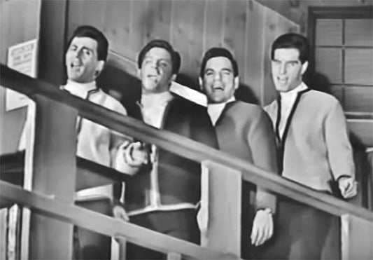 Black and white photo of a male vocal group singing together while standing on a staircase, dressed in matching outfits.