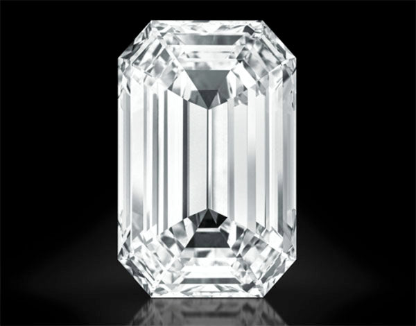Close-up of a large, clear emerald-cut diamond with multiple facets, reflecting light against a black background.