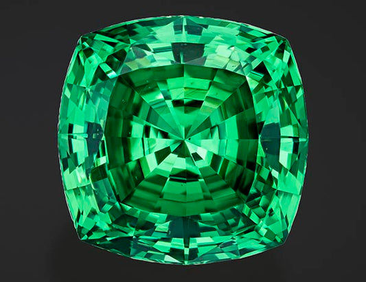Large, brilliant green emerald gemstone with a square cushion cut, showcasing intricate facets and deep color.