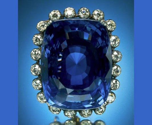 Large blue sapphire gemstone surrounded by a halo of diamonds, set against a blue background.