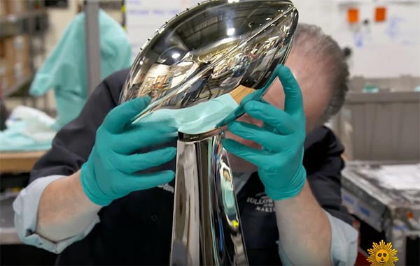 Close-up of a worker polishing the iconic Super Bowl trophy, wearing protective gloves in a manufacturing facility.