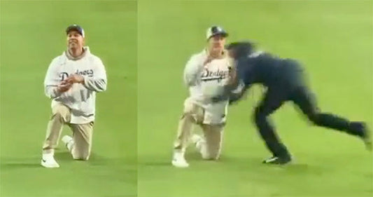 Man in Dodgers hoodie on the field kneels as a security guard tackles him during a baseball game.
