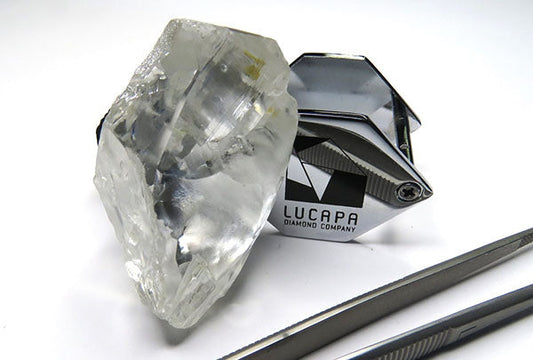 Large rough diamond from Lucapa Diamond Company next to a branded diamond tweezers tool, showcasing the raw form of the crystal.