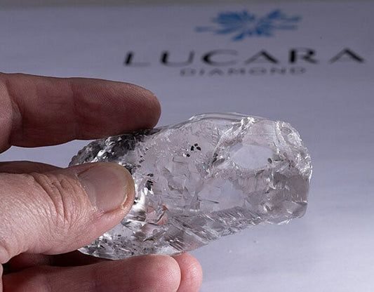 Hand holding a large raw diamond from Lucara Diamond, showcasing its rough, uncut form with intricate internal inclusions.