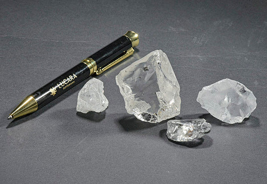 Rough diamond crystals next to a pen, with the diamonds displayed on a dark surface for comparison, highlighting their raw, uncut form.