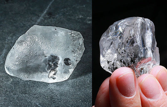 A large raw diamond being held in hand, showing a rough, uncut crystal with visible inclusions and imperfections.