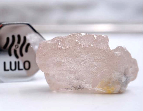 Large rough pink diamond crystal next to a Lulo gemological identification tag, showcasing its natural form and clarity.