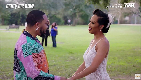 Couple holding hands and smiling at each other during a romantic moment outdoors, featured in the show 'Marry Me Now' on OWN network.