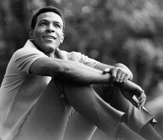 Black and white image of Marvin Gaye sitting with a relaxed expression, wearing a polo shirt and looking up with a smile.