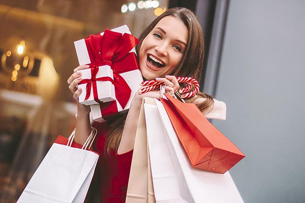 Happy woman holding holiday gifts and shopping bags, with Christmas presents and candy canes, standing outside a store.