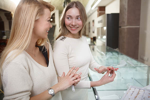 Two women smiling and admiring jewelry at a store, trying on rings from a display case, with a bright and elegant setting
