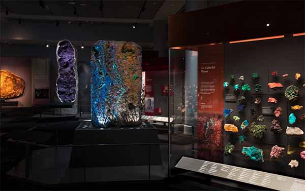Colorful mineral display at a museum featuring large illuminated rocks and a collection of vibrant gemstones and crystals in display cases.
