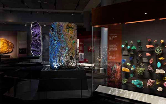 Colorful mineral display at a museum featuring large illuminated rocks and a collection of vibrant gemstones and crystals in display cases.