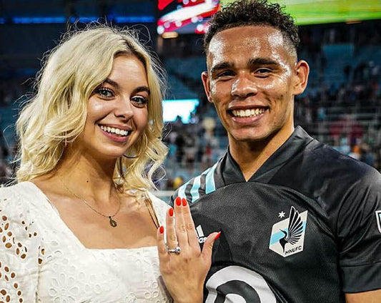 Couple celebrating an engagement after a soccer match, with the woman showing off her engagement ring while standing beside her partner, a professional soccer player wearing his team jersey.