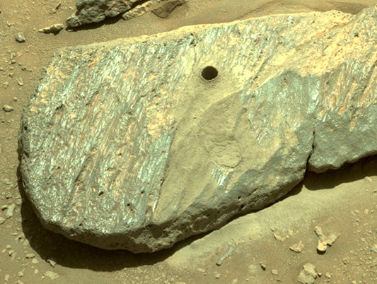 Close-up of a rock with a hole in the surface, showing distinct mineral layers and textures, captured by the Mars rover.
