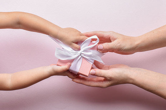 A child and an adult exchanging a pink gift box tied with a white satin ribbon, symbolizing love and sharing.