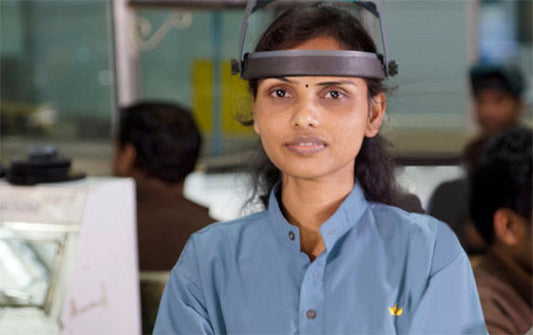 Female factory worker wearing protective visor and blue uniform, standing in a manufacturing environment.
