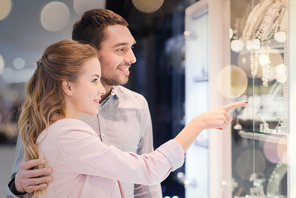 Couple admiring jewelry in a store, with the woman pointing at a display case filled with sparkling bracelets and necklaces.