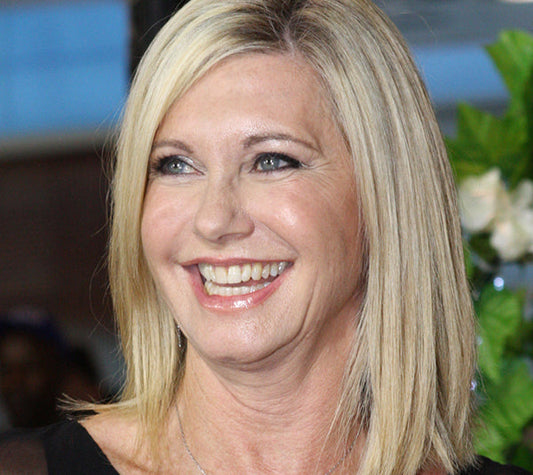 Olivia Newton-John smiling with her blonde hair styled in a bob, wearing a black dress, and a bright, cheerful expression.