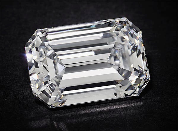 Large, clear, emerald-cut diamond with sharp facets, showcasing brilliance and clarity against a dark background.