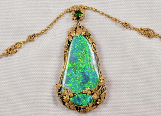 Vintage gold pendant with a large opal gemstone surrounded by intricate floral design, featuring green accents and sparkling details.