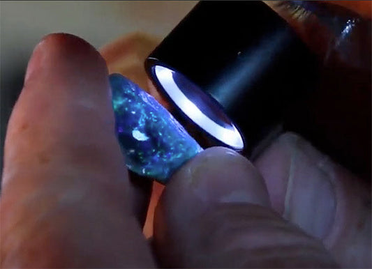 Close-up of a person examining a colorful opal gemstone under a jeweler's loupe with a magnifying light.
