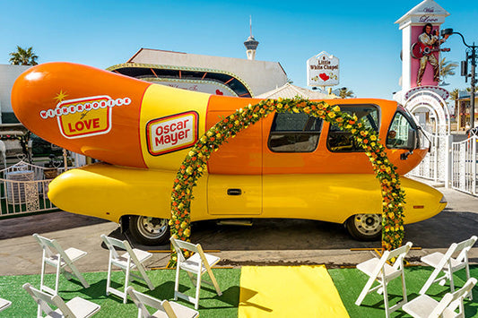 Colorful Oscar Mayer Wienermobile decorated with flowers at a wedding venue in Las Vegas with white chairs and a yellow carpet.