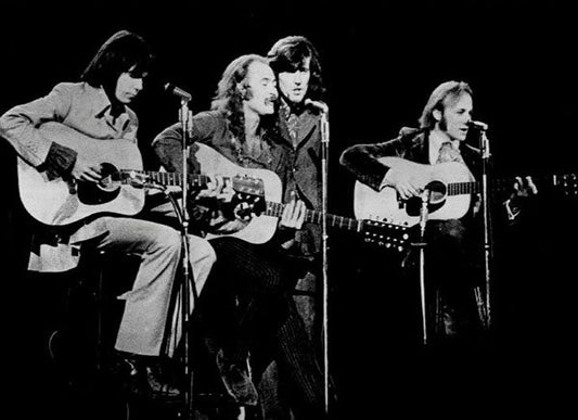 Classic black and white photo of Crosby, Stills, Nash & Young performing live on stage with acoustic guitars.