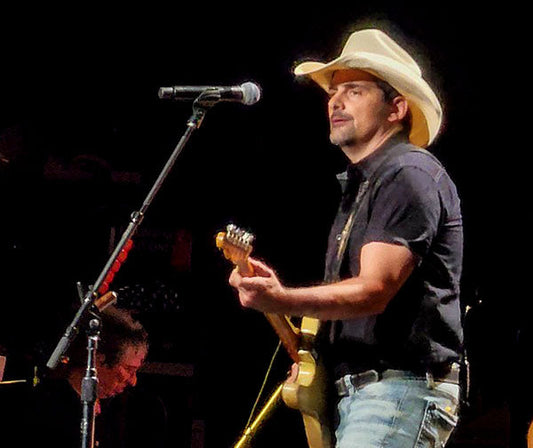 Brad Paisley performing on stage with a guitar, wearing a cowboy hat during a live concert.