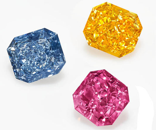 Three colorful gemstones including a blue diamond, yellow diamond, and pink diamond, each with an intricate faceted cut, placed on a white background.